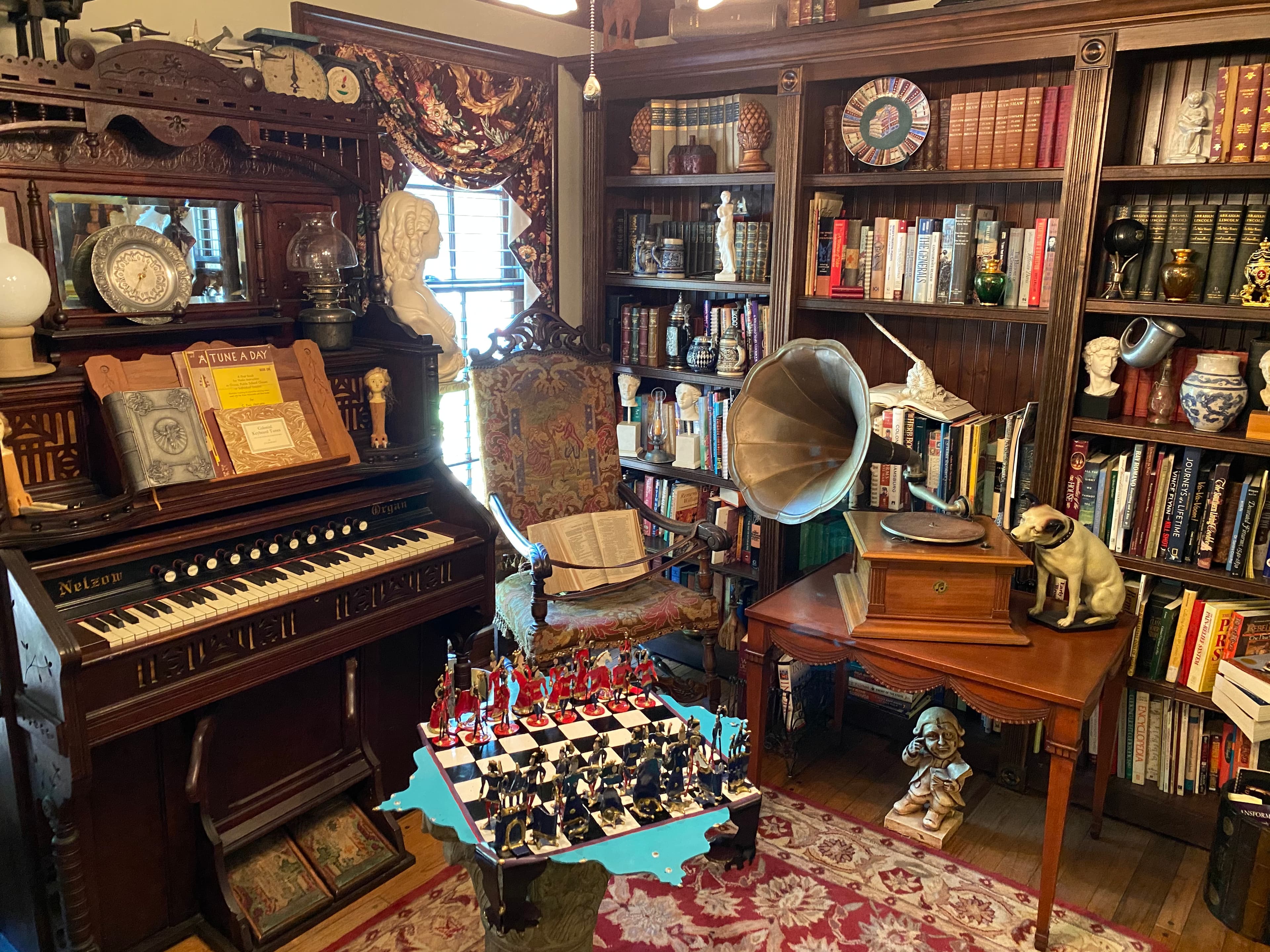 A cozy vintage library featuring a piano, gramophone, intricately designed furniture, and a chess set on a decorative rug.