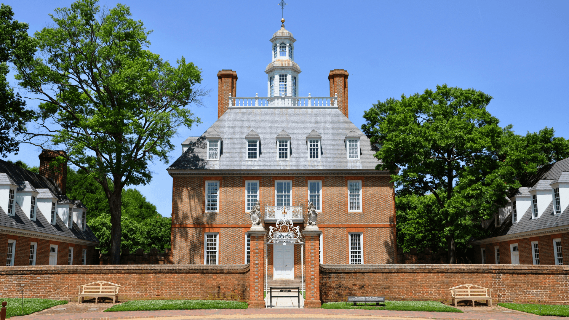 Historical building with a central tower, surrounded by greenery and benches.