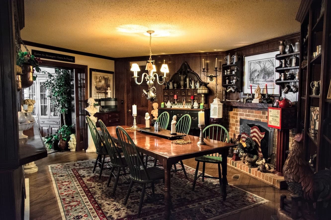 A cozy dining room featuring a wooden table, green chairs, decorative items, and a fireplace.