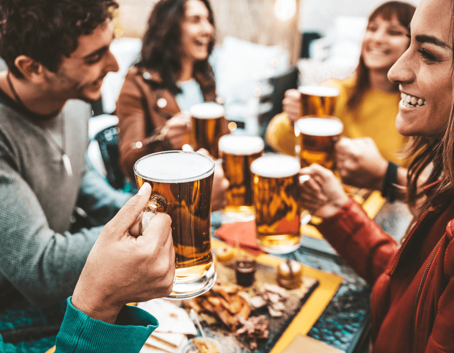 A group of friends joyfully raising mugs of beer around a table with food.