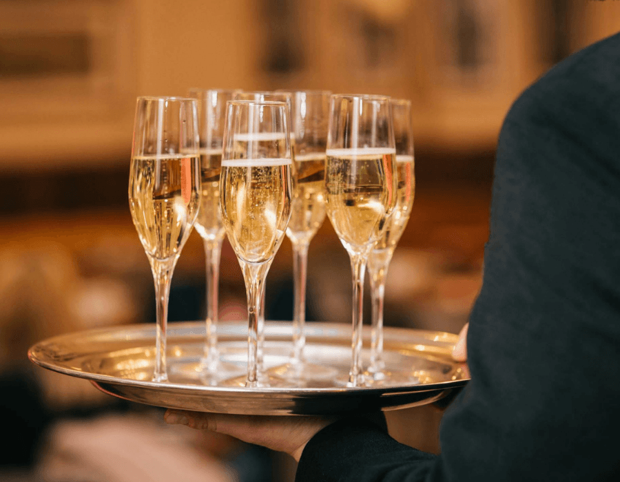 A server holds a silver tray with several glasses of champagne.
