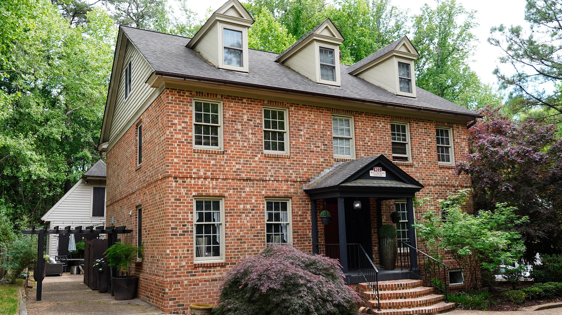 A brick two-story house surrounded by green trees and shrubs.