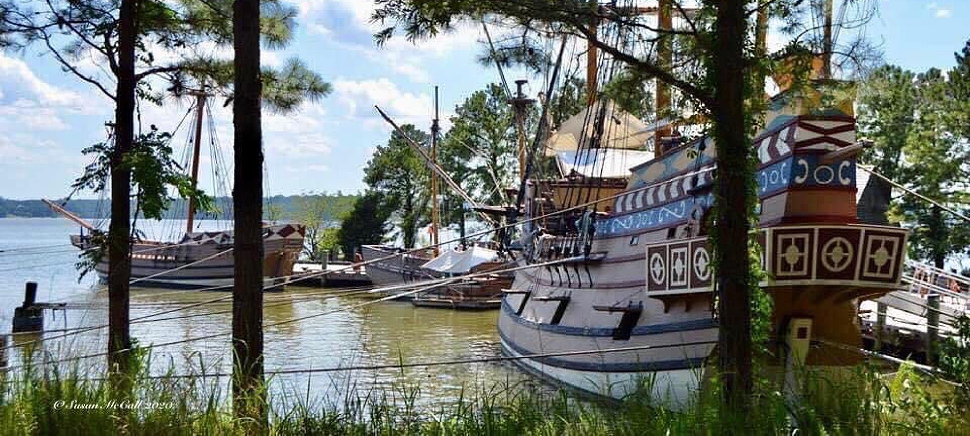 Three pirate style ships docked by a path surrounded by trees