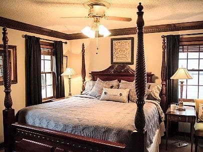 Bedroom with mahogany four poster bed with two windows with curtains