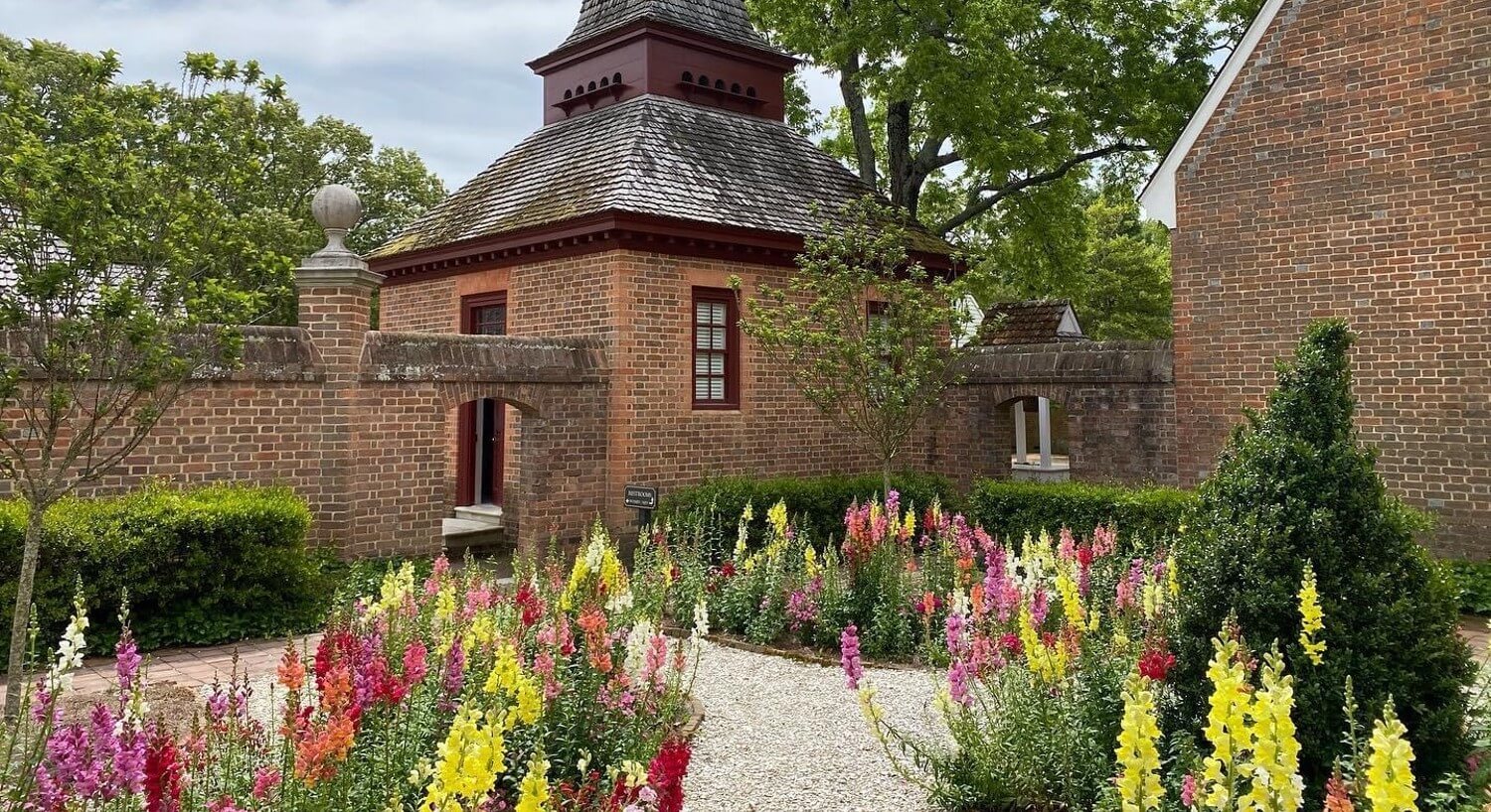 Historic brick building with gravel walkway through a garden of brightly colored flowers