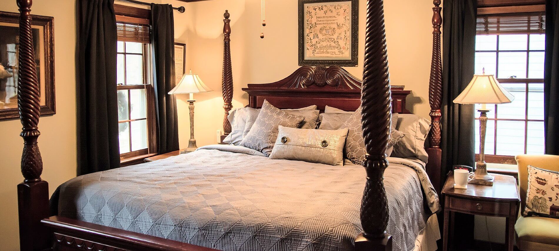 Elegant bedroom with four poster bed, side tables with lamps, sitting chair and two windows