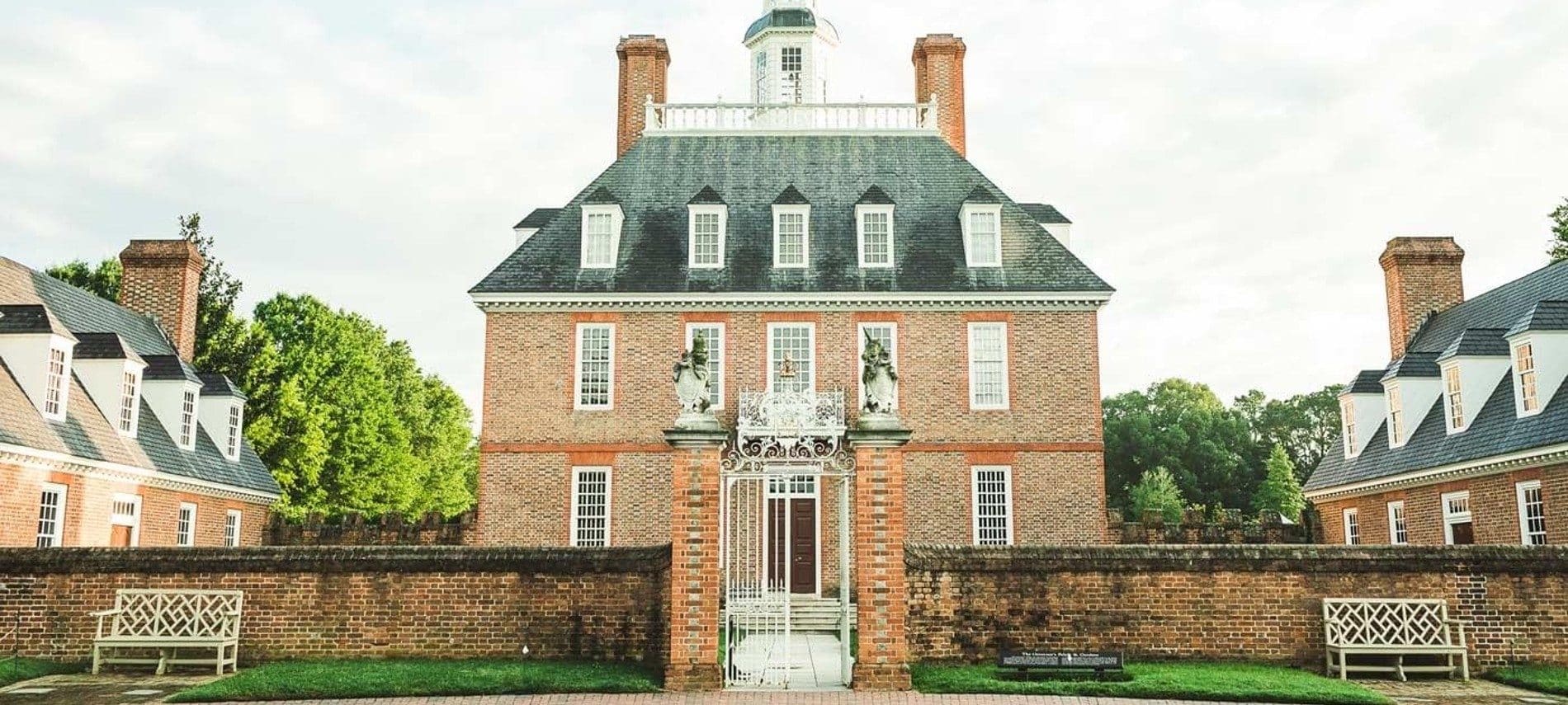 Front facade of a historic home behind a brick wall and flanked by two similar buildings