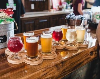 Flight of small glasses of different types of beer sitting on a wooden counter