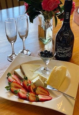 Plate with fruit and cheese next to bottle of wine and two wine glasses